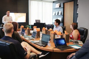 Team attending a business presentation in a conference room with laptops and gift bags on the table.