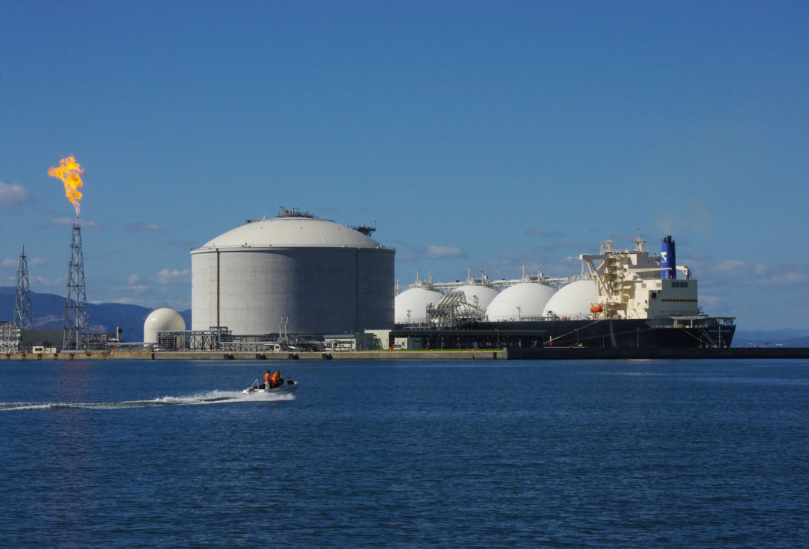 An LNG carrier unloading at an onshore import and regasification terminal with storage tanks